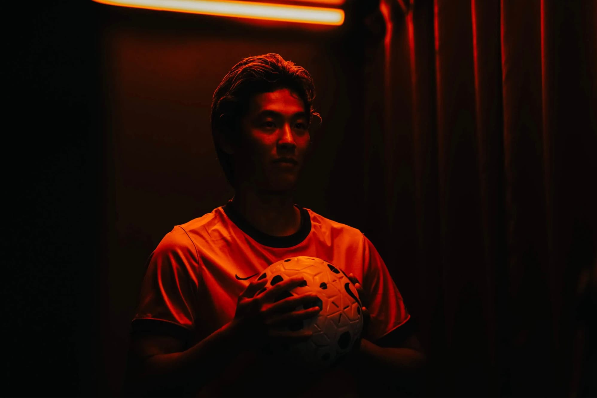 Joueur tenant un ballon de football dans un couloir éclairé