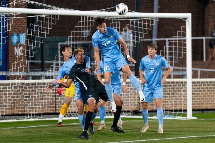 Joueur en maillot bleu disputant un ballon de la tête devant le but